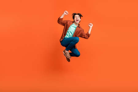 Full size photo of excited crazy smiling male jumping raise fists in victory triumph isolated on orange color backgroundの写真素材