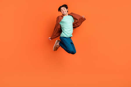 Full size photo of funky smiling cheerful carefree man jumping enjoy summer vacation isolated on orange color backgroundの写真素材