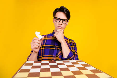 Photo of millennial think guy play chess wear checkered shirt spectacles isolated on yellow color backgroundの写真素材