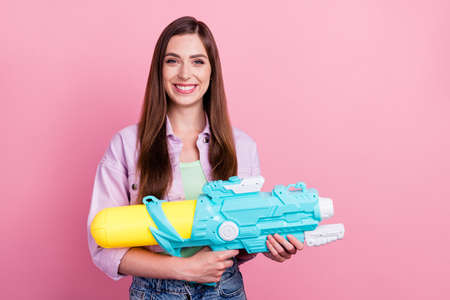 Photo portrait woman smiling playful keeping water blaster isolated pastel pink color backgroundの写真素材