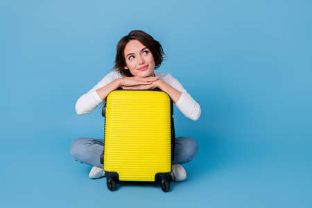 Photo of funny thoughtful woman wear white shirt hugging luggage looking empty space isolated blue color backgroundの写真素材