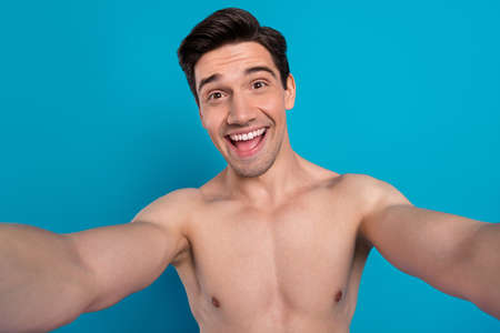 Photo of pretty excited young guy topless smiling recording self video isolated blue color backgroundの写真素材