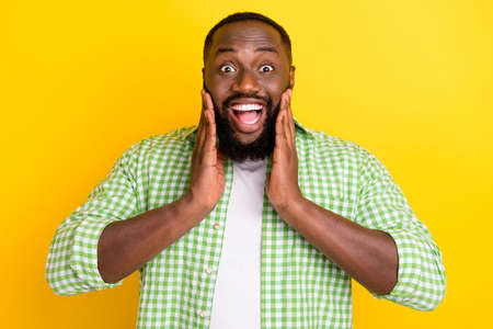 Portrait of astonished cheerful person arms on cheeks open mouth incredible reaction isolated on yellow color backgroundの写真素材