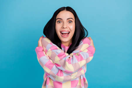 Photo of sweet excited young woman wear pink sweater open mouth embracing herself isolated blue...