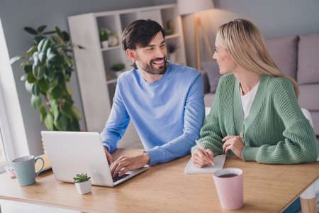 Portrait of two attractive cheerful people using laptop watching video service tutorial at home indoorsの写真素材
