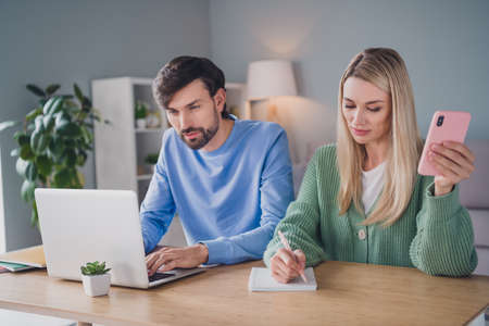 Photo of focused busy entrepreneurs quarantine work use netbook lady write to-do list hold smart phone sit table apartment roomの写真素材