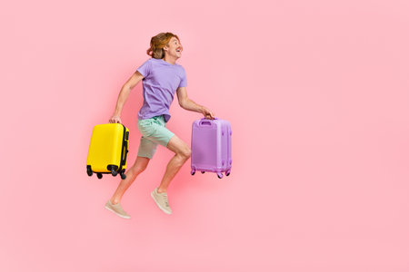 Full length body size view of attractive cheery guy jumping holding bags running low cost flight isolated over pink pastel color backgroundの写真素材