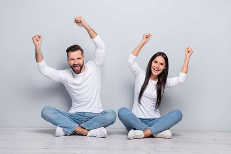 Photo of lucky funny brother sister wear white shirts rising fists isolated concrete grey wall backgroundの写真素材
