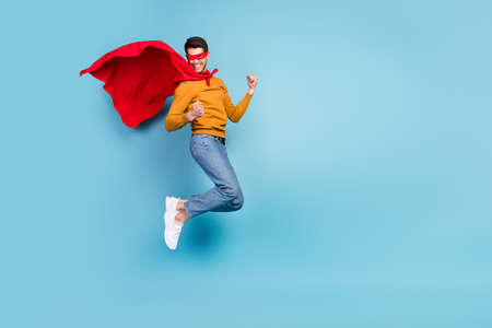 Photo of charming lucky guy dressed pullover man costume jumping rising fists empty space smiling isolated blue color backgroundの写真素材