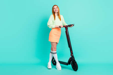Photo of cute adorable young lady dressed green outfit walking scooter looking empty space isolated turquoise color backgroundの写真素材