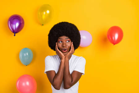 Photo of attractive afro american nice dream shocked lady look empty space hands cheeks balloons isolated on yellow color backgroundの写真素材