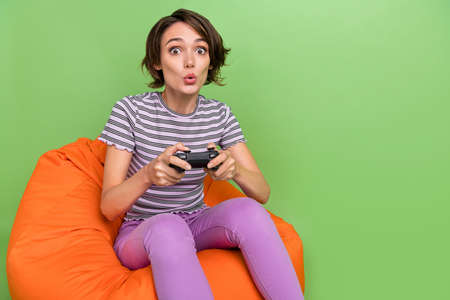 Photo of cool millennial brunette lady play game sit on bag wear t-shirt jeans isolated on green...
