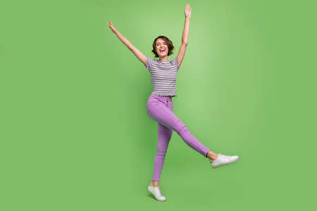 Full length photo of cool young brunette lady dance wear t-shirt jeans sneakers isolated on green...