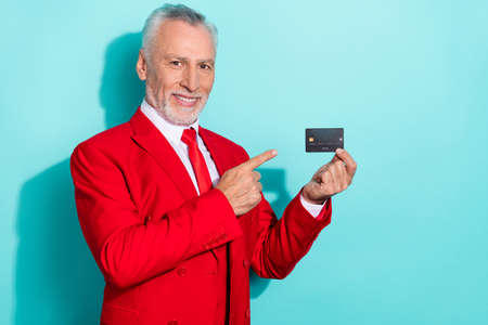 Photo of charming retired man wear red three piece suit pointing bank card isolated turquoise color backgroundの写真素材