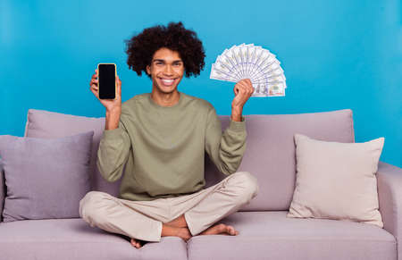 Full body photo of young man hold mobile cash bet earnings benefit wealthy isolated over blue color...