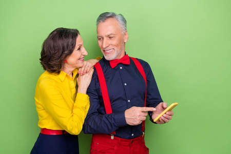 Photo of two peaceful elderly partners direct finger show telephone isolated on green color...