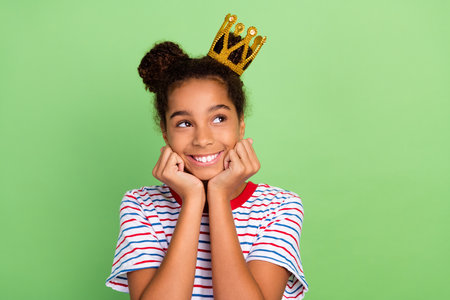 Photo of young black preteen lady happy positive smile princess dream look empty space isolated over green color backgroundの写真素材