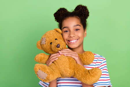 Photo of young african little girl happy positive smile play toy teddy bear isolated over green color backgroundの写真素材