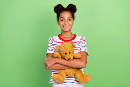 Portrait of attractive cheerful brunet girl hugging childish bear isolated over green pastel color backgroundの写真素材