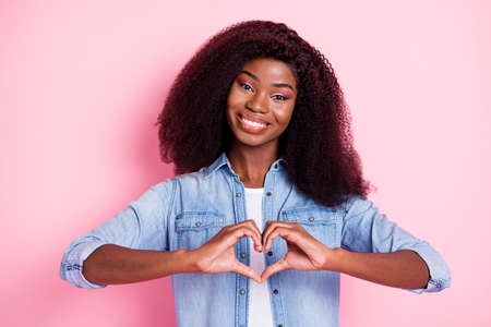 Portrait of attractive cheerful wavy-haired girl showing heart shape isolated over pink pastel color backgroundの写真素材