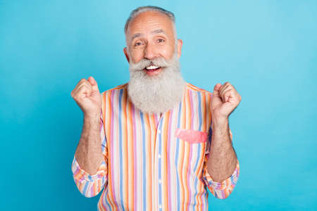 Photo of aged man happy positive smile rejoice victory success fists hands isolated over blue color backgroundの写真素材