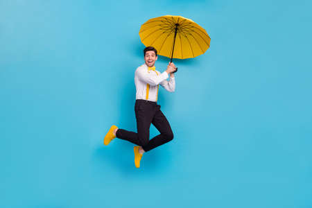 Full body photo of excited satisfied person hold umbrella fly isolated on blue color backgroundの写真素材