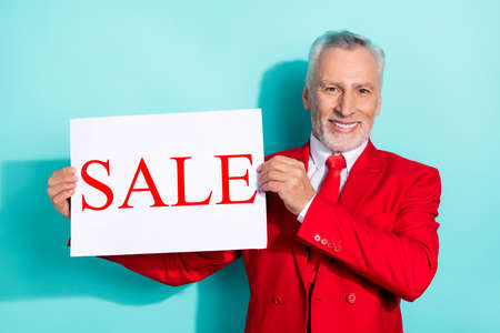 Photo of charming man pensioner dressed red three piece tux holding sale placard isolated teal color backgroundの写真素材