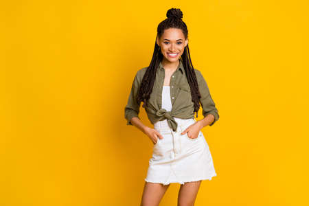 Photo portrait of cheerful girl holding two hands in pockets isolated on vivid yellow colored background with blank spaceの写真素材