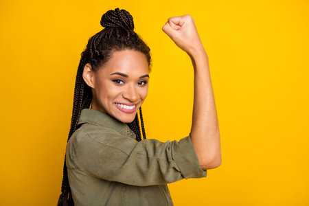 Photo portrait of african american girl flexing biceps isolated on vivid yellow colored background