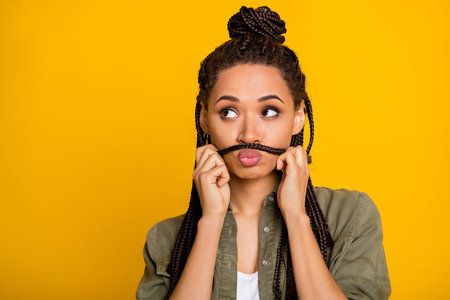 Portrait of pretty dark skin person hands play with tail make mustache look empty space isolated on yellow color backgroundの写真素材