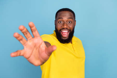 Photo of shocked funny dark skin man wear yellow t-shirt smiling showing palm isolated blue color...
