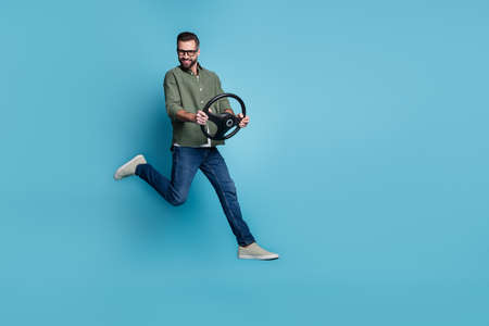 Full size photo of cheerful handsome male jumping traveling hold car steering wheel isolated on blue...