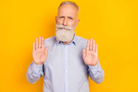 Photo of serious confident age gentleman wear blue shirt showing palms ask stop isolated yellow color backgroundの写真素材