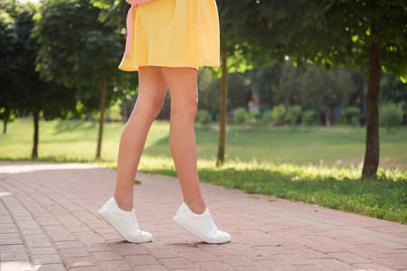 Cropped photo of young girl wear short skirt legs slim wear sneakers walk park nature summer green treesの写真素材