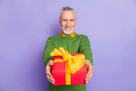 Photo of charming retired man wear green sweater presenting you gift box isolated violet color...