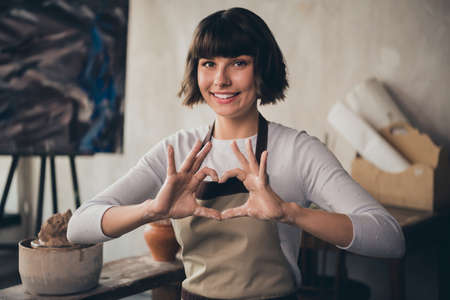 Photo of self-employed lady small store owner potter make heart shape enjoy life vocation hobby sit in workroomの写真素材