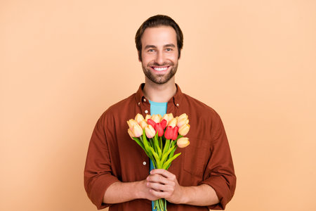 Photo of confident charismatic boyfriend prepare date hold bunch flowers wear casual outfit isolated beige color backgroundの写真素材