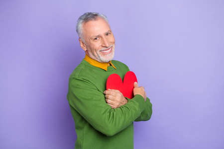 Photo of pretty retired man wear green sweater embracing large red heart isolated violet color backgroundの写真素材