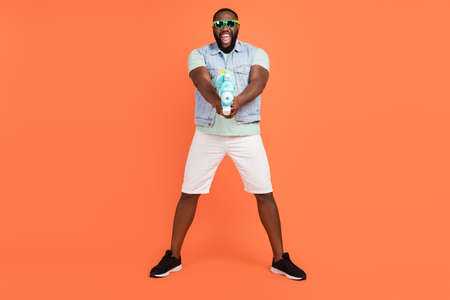 Photo of funny impressed guy dressed jeans waistcoat dark glasses shooting water gun isolated orange...