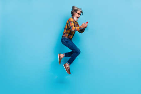 Photo of excited retired man wear plaid shirt spectacles jumping high typing modern device isolated...