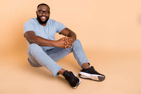 Portrait of attractive cheerful guy sitting on floor resting copy space isolated over beige pastel color backgroundの写真素材