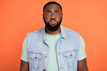 Photo of abused african guy dressed jeans waistcoat bloated cheeks isolated orange color background