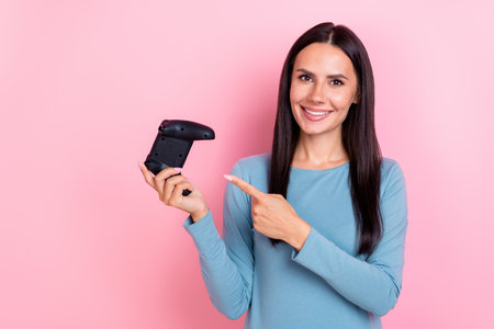 Photo of pretty charming lady dressed blue shirt pointing finger to game controller isolated pink...