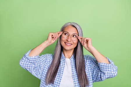 Photo of cute aged white hairdo lady look empty space wear spectacles blue shirt isolated on green color backgroundの写真素材
