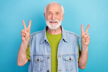 Photo of funny charming man pensioner dressed retro denim vest smiling showing two v-signs isolated...