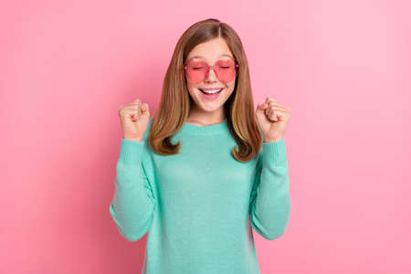 Photo of lucky girl wear turquoise sweater heart glasses rising fists isolated pink color backgroundの写真素材