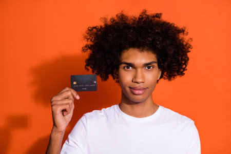 Photo of attractive handsome guy dressed white shirt showing you credit card isolated orange color backgroundの写真素材