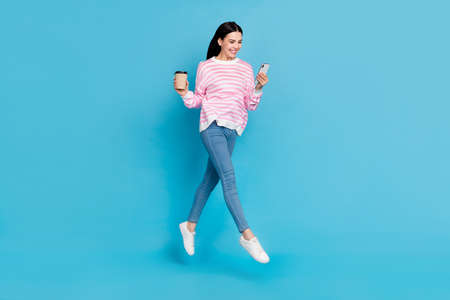 Full body photo of young girl look mobile like post share drink latte caffeine break isolated over blue color backgroundの写真素材