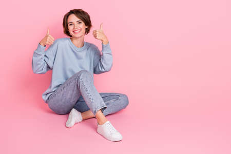 Full length photo of positive adorable lady sit floor two arms show thumbs up isolated on pink color backgroundの写真素材