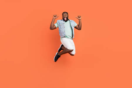 Photo of amazed afro guy wear denim vest jumping high pointing himself isolated orange color backgroundの写真素材